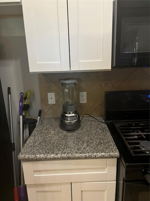 kitchen featuring black appliances, decorative backsplash, white cabinetry, and light stone countertops