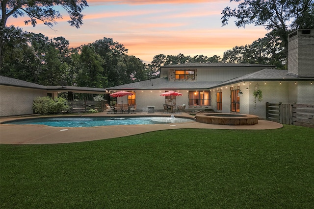 pool at dusk with a lawn, a patio area, and an in ground hot tub