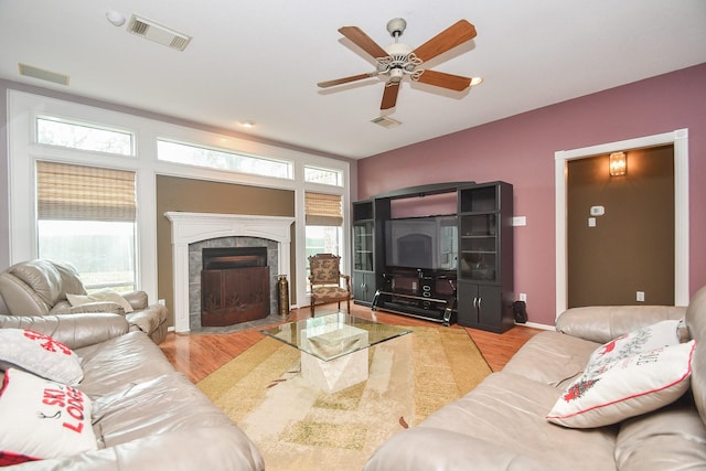 living room featuring ceiling fan, light wood-type flooring, a wealth of natural light, and a tiled fireplace