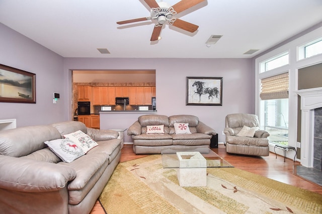 living room featuring a tile fireplace, light hardwood / wood-style flooring, and ceiling fan