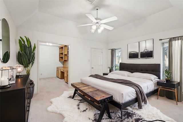 bedroom with ceiling fan, vaulted ceiling, light colored carpet, and a tray ceiling