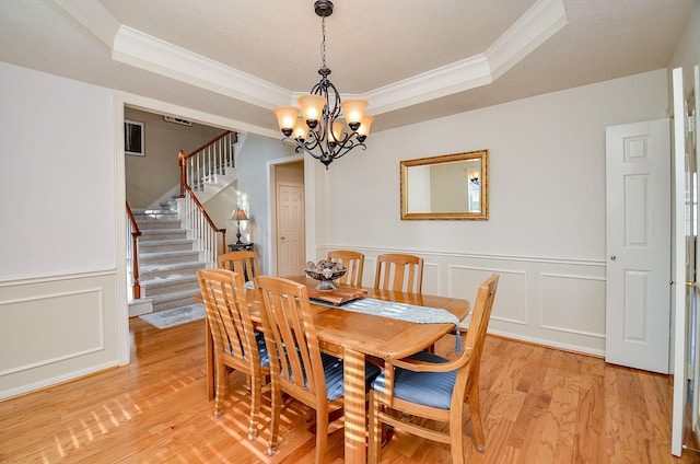 dining space featuring an inviting chandelier, a raised ceiling, ornamental molding, a textured ceiling, and light hardwood / wood-style floors