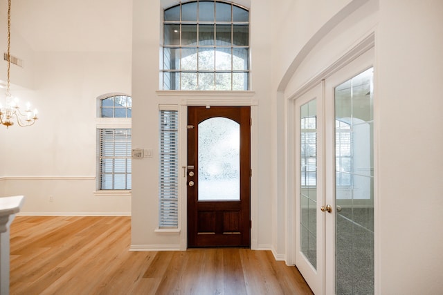 entryway with hardwood / wood-style floors, a towering ceiling, a chandelier, and french doors