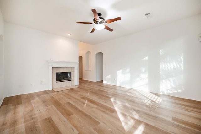 unfurnished living room featuring a tile fireplace, ceiling fan, and light wood-type flooring