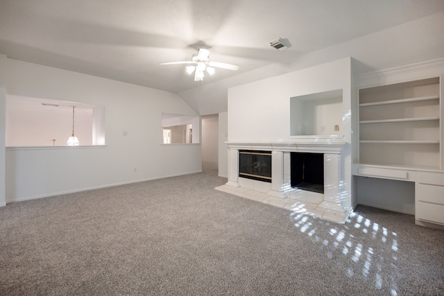 unfurnished living room with a tile fireplace, ceiling fan, built in shelves, light colored carpet, and built in desk