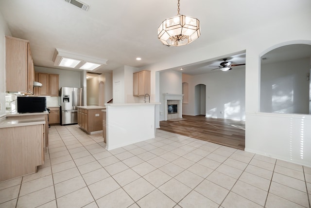 kitchen with light brown cabinets, a center island, stainless steel fridge, decorative light fixtures, and light wood-type flooring