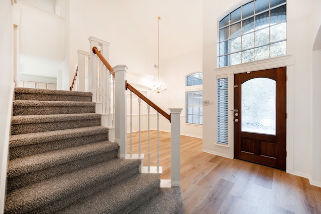 foyer entrance featuring hardwood / wood-style floors, a towering ceiling, and an inviting chandelier