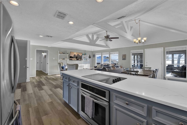 kitchen with pendant lighting, vaulted ceiling with beams, light stone countertops, a textured ceiling, and appliances with stainless steel finishes