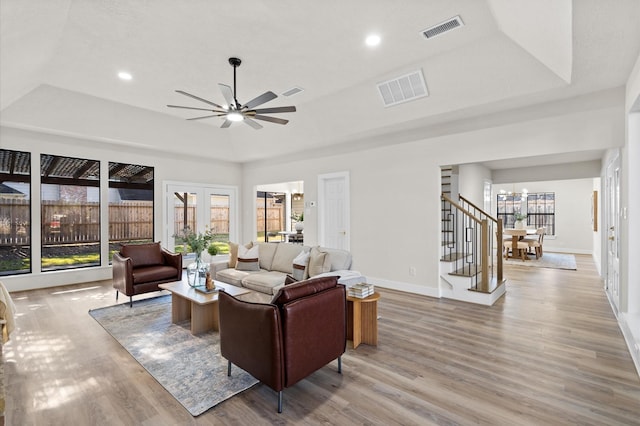 living room with a raised ceiling, ceiling fan, and light hardwood / wood-style flooring