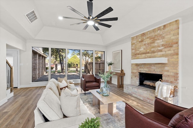 living room featuring ceiling fan, a brick fireplace, a raised ceiling, vaulted ceiling, and light wood-type flooring