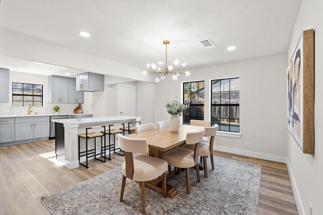 dining room featuring a textured ceiling, light hardwood / wood-style floors, a notable chandelier, and sink