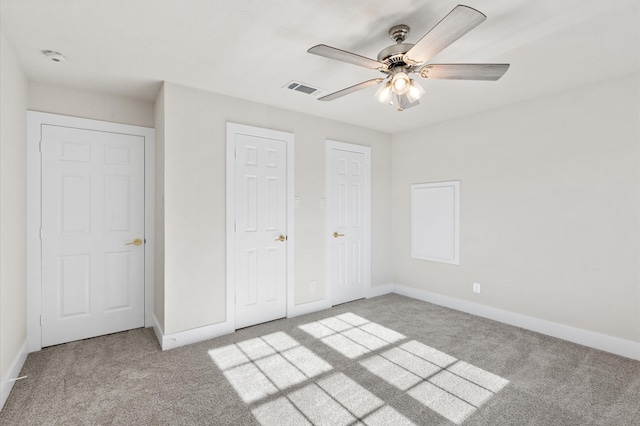 unfurnished bedroom with ceiling fan, light colored carpet, and two closets