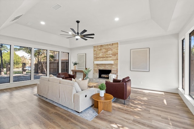 living room featuring a large fireplace, light hardwood / wood-style floors, a wealth of natural light, and a tray ceiling