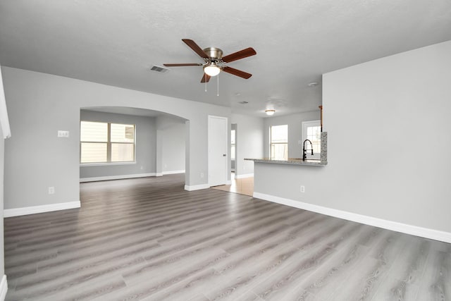 unfurnished living room with a textured ceiling, light hardwood / wood-style flooring, ceiling fan, and sink