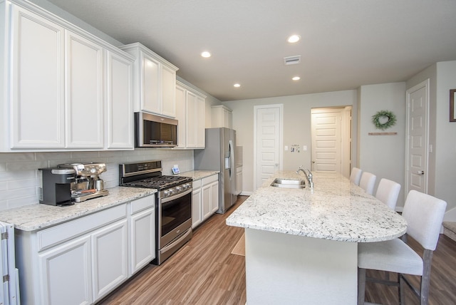 kitchen featuring a kitchen island with sink, white cabinets, light wood-type flooring, appliances with stainless steel finishes, and a breakfast bar area