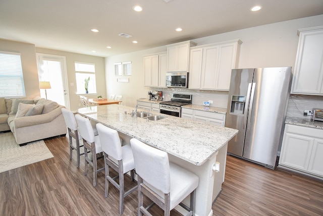 kitchen with appliances with stainless steel finishes, tasteful backsplash, dark wood-type flooring, white cabinetry, and an island with sink