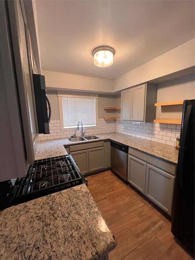 kitchen featuring backsplash, black appliances, sink, light stone countertops, and light hardwood / wood-style floors