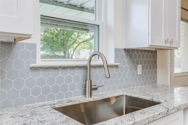 kitchen featuring tasteful backsplash, light stone counters, sink, and white cabinets