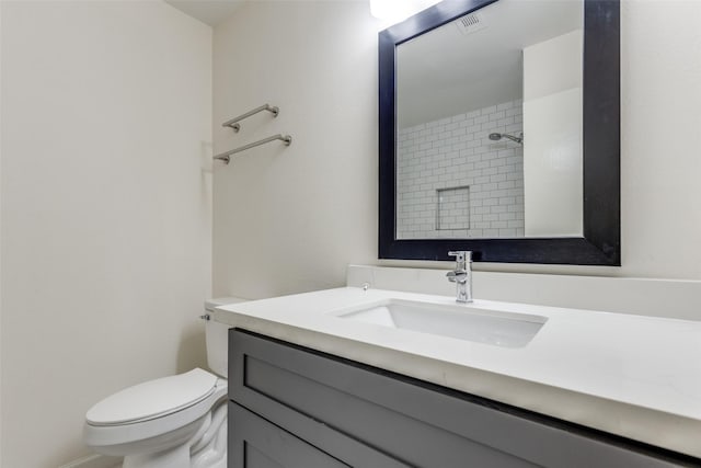 bathroom with a tile shower, vanity, and toilet