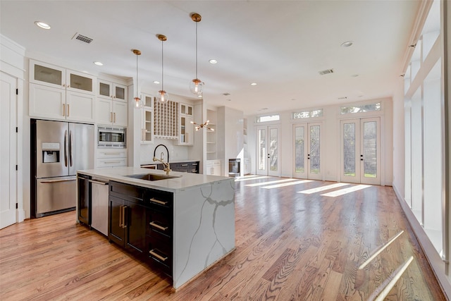 kitchen with pendant lighting, white cabinets, a center island with sink, sink, and appliances with stainless steel finishes