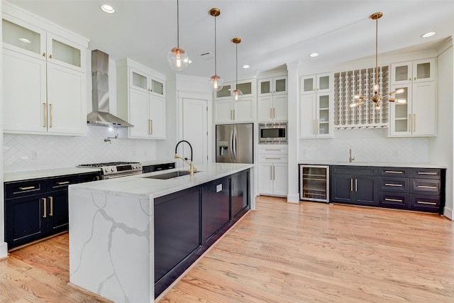 kitchen featuring white cabinetry, an island with sink, wall chimney range hood, and appliances with stainless steel finishes