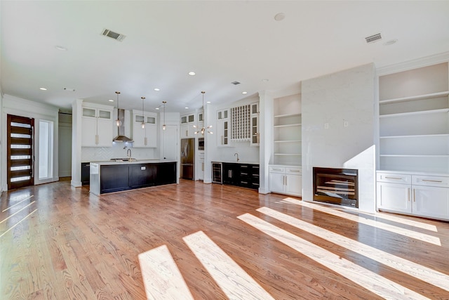 unfurnished living room featuring built in shelves, crown molding, sink, and light hardwood / wood-style flooring