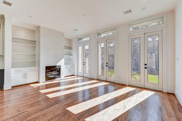 unfurnished living room featuring light wood-type flooring, built in features, a fireplace, and french doors