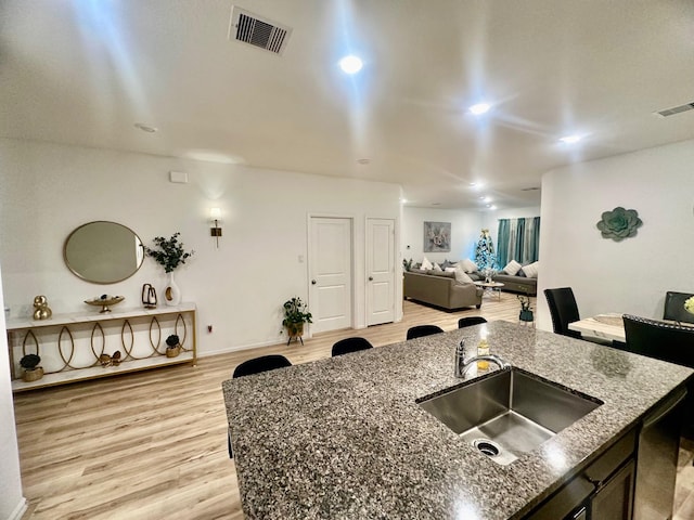 kitchen with a kitchen island with sink, sink, dark stone counters, and light wood-type flooring