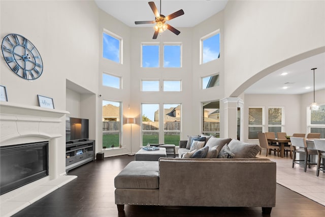 living room with a wealth of natural light, dark wood-type flooring, and ceiling fan