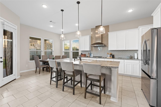 kitchen featuring white cabinets, hanging light fixtures, wall chimney exhaust hood, an island with sink, and stainless steel appliances