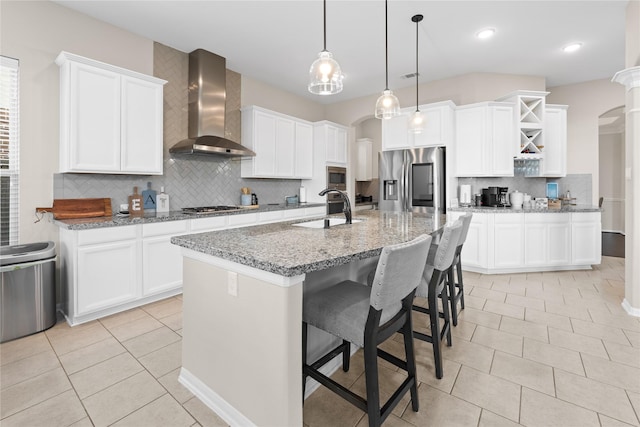 kitchen featuring wall chimney exhaust hood, stainless steel appliances, sink, pendant lighting, and a center island with sink