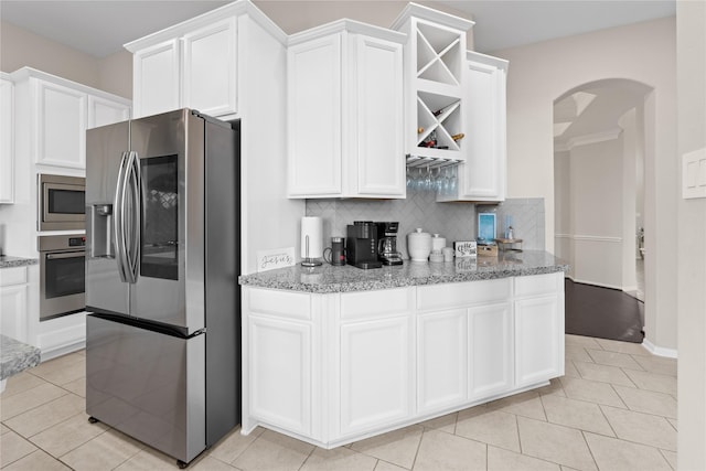 kitchen with backsplash, light stone countertops, appliances with stainless steel finishes, light tile patterned flooring, and white cabinetry