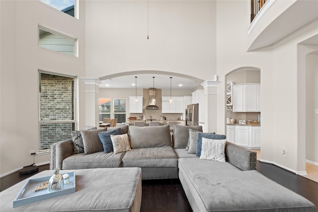 living room featuring dark hardwood / wood-style floors, a towering ceiling, and ornate columns