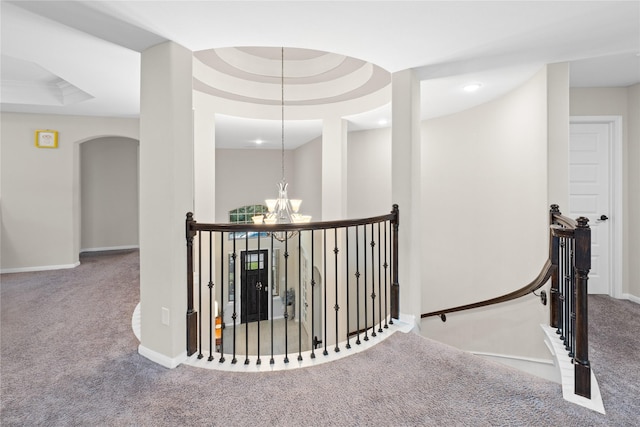 corridor with a tray ceiling, light colored carpet, and an inviting chandelier