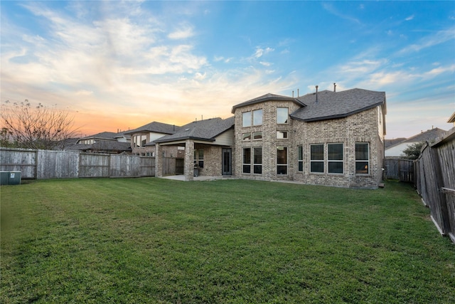 back house at dusk featuring a lawn and a patio area