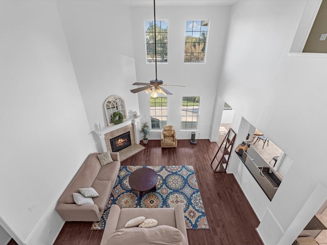 living room featuring a premium fireplace, dark wood-type flooring, a towering ceiling, and a healthy amount of sunlight