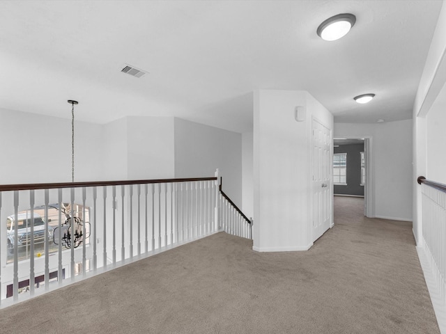 hall with light colored carpet and an inviting chandelier