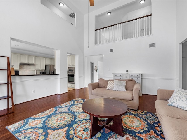 living room featuring ceiling fan, dark wood-type flooring, and a high ceiling