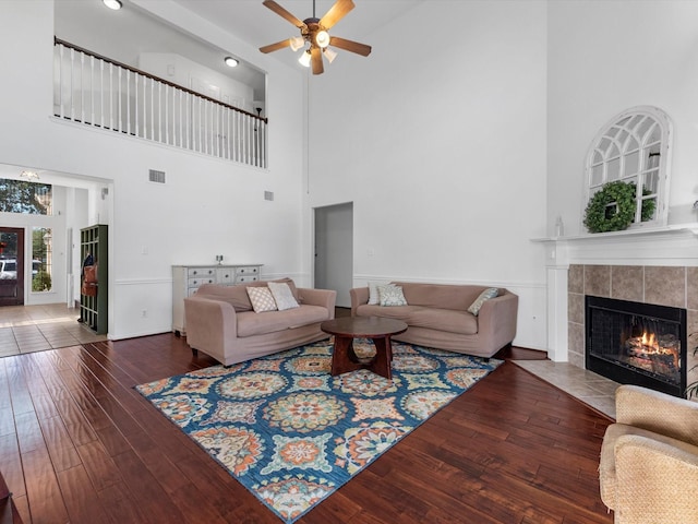 living room with ceiling fan, dark hardwood / wood-style flooring, a towering ceiling, and a tile fireplace