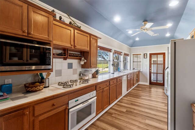 kitchen featuring tile countertops, white appliances, lofted ceiling, light hardwood / wood-style flooring, and tasteful backsplash