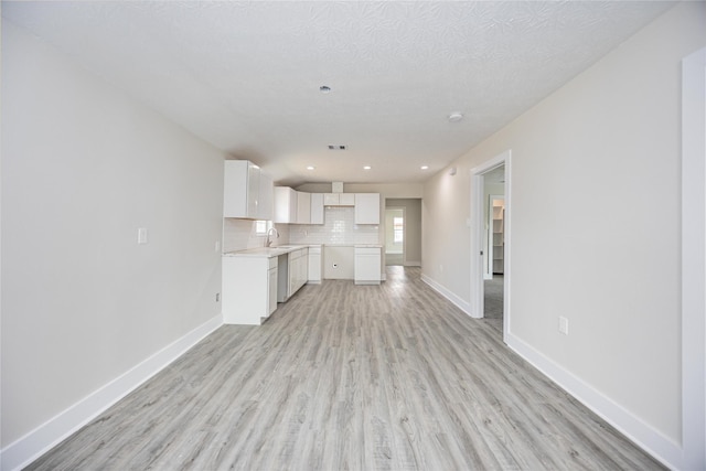 kitchen with stainless steel dishwasher, light hardwood / wood-style floors, a textured ceiling, decorative backsplash, and white cabinets