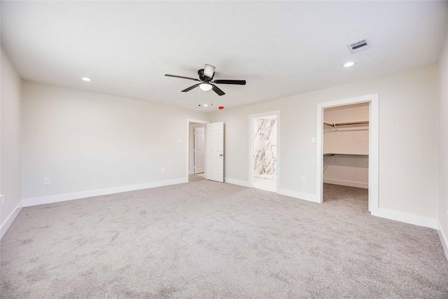 unfurnished bedroom with a spacious closet, ceiling fan, ensuite bathroom, light carpet, and a closet