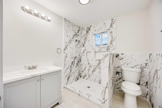 bathroom featuring a shower, vanity, toilet, and tile walls