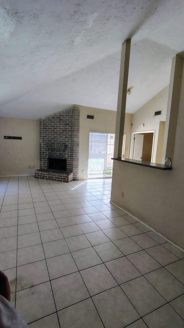 unfurnished living room with vaulted ceiling, ceiling fan, light tile patterned floors, and a fireplace