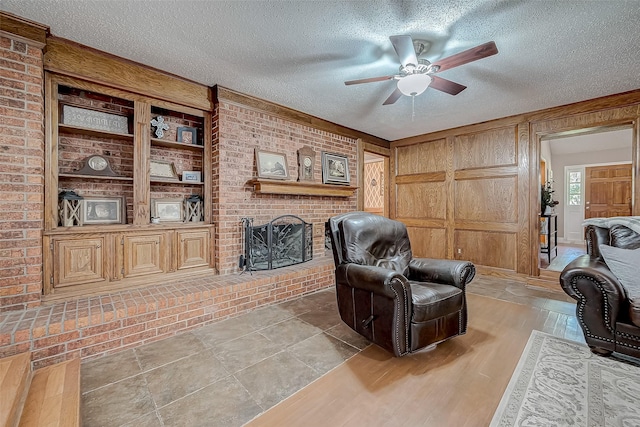 tiled living room featuring a fireplace, a textured ceiling, ceiling fan, and brick wall