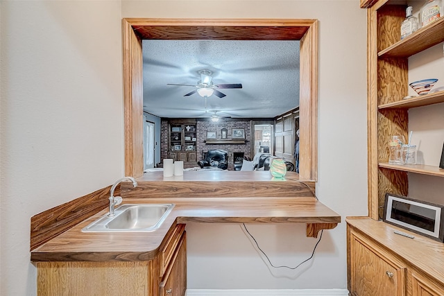 kitchen featuring a textured ceiling, a brick fireplace, ceiling fan, and sink