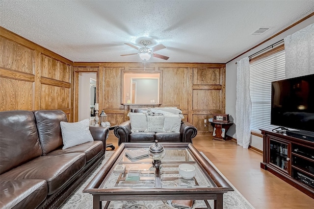 living room featuring wood walls, ornamental molding, a textured ceiling, and light wood-type flooring