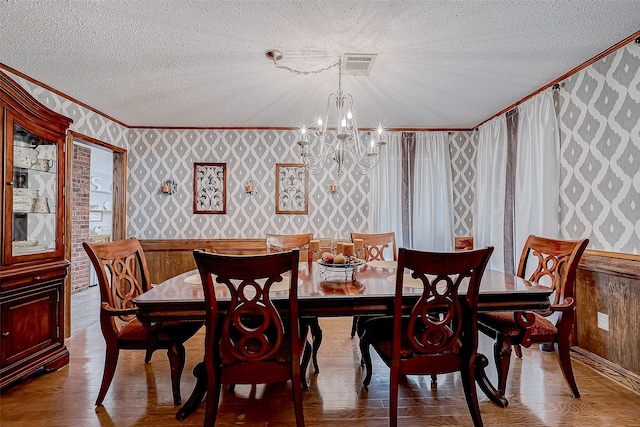 dining space with a textured ceiling, light wood-type flooring, an inviting chandelier, and crown molding