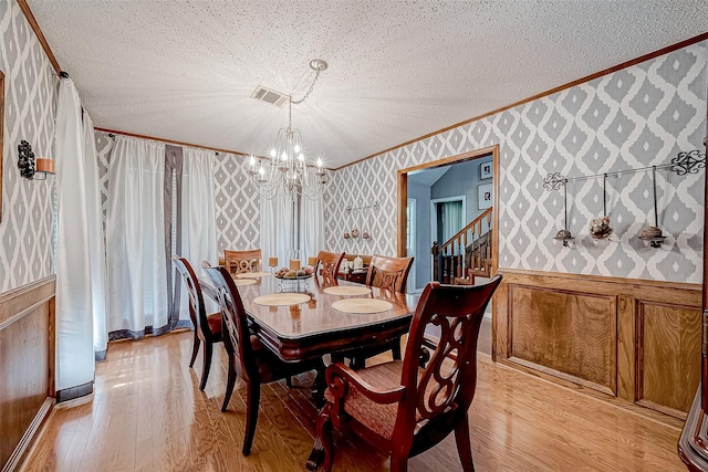 dining room with ornamental molding, light wood-type flooring, a textured ceiling, and an inviting chandelier