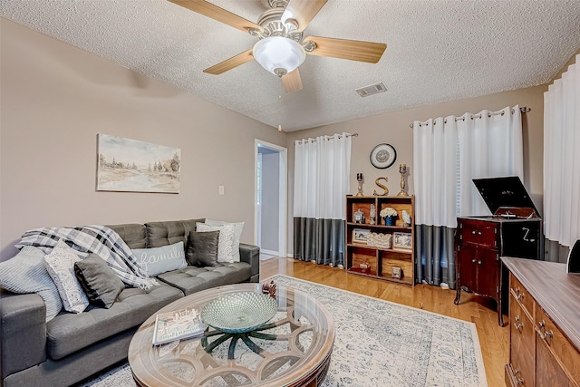 living room featuring ceiling fan, light wood-type flooring, and a textured ceiling